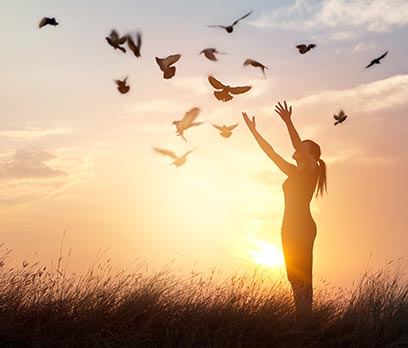 Photo d'une femme qui lèbre des oiseaux dans u nchamp au soleil couchant, coach santé et épanouissement